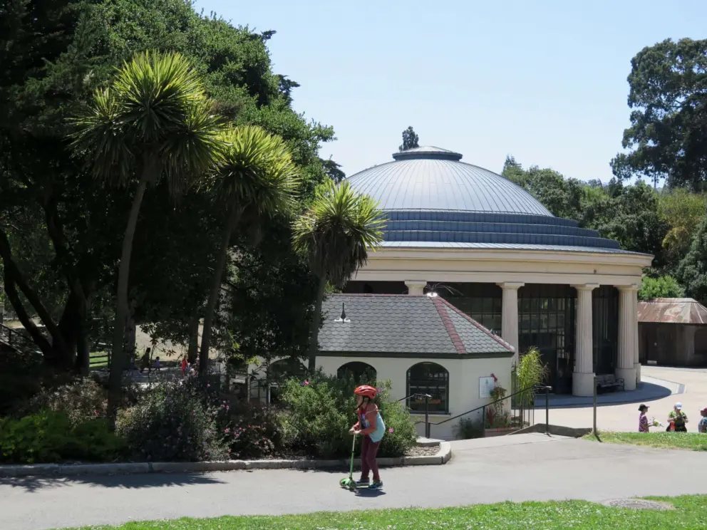 A girl scooters by the carousel building.