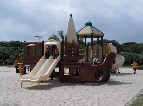 Wide-open beach with pale grey sand, shells on the shore, and aquamarine water, across from a playground, turtle center, and hike.