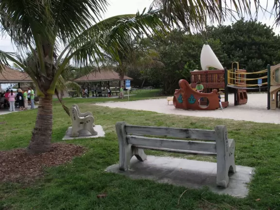 Wide-open beach with pale grey sand, shells on the shore, and aquamarine water, across from a playground, turtle center, and hike.