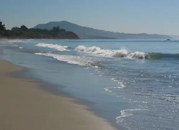 A curved beach and a clifftop park with playground and picnic tables.