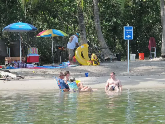 People sitting on beach chairs in the water on a 90 degree day.