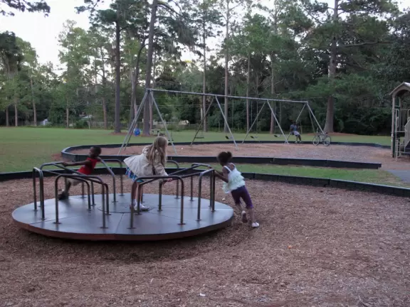 Spacious park with tall trees, merry-go-round, swings, and playground.