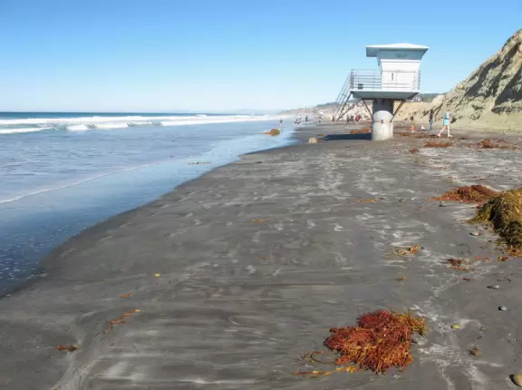 Beach with sparkling black sand, and hike atop high red cliffs with views.