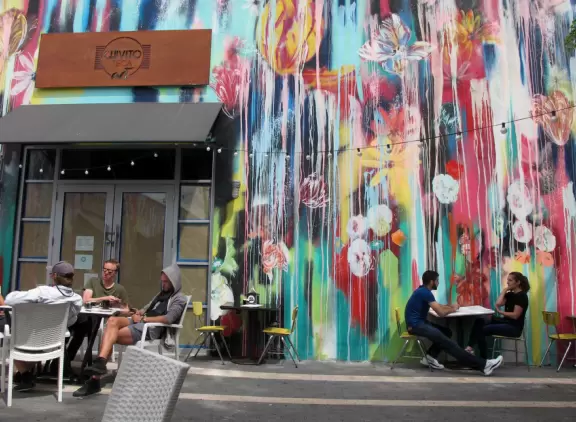 A trendy street in the middle of a sketchy neighborhood, with cafes and colorful graffiti-covered walls.