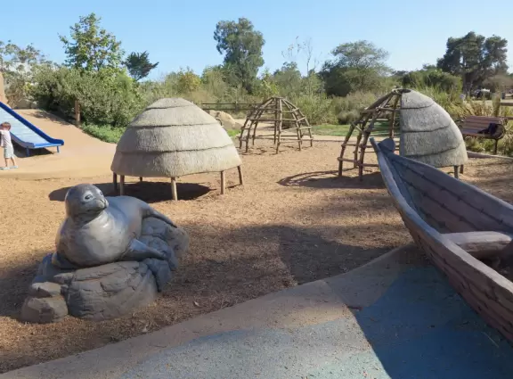 Modern playground with Chumash Indian huts and canoe, seals and whales to climb, roller slide, rainbow bridge, and bald eagle in a nest.