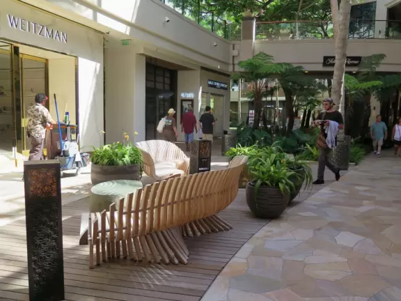 An outdoor mall under a huge banyan tree hung with lanterns. Beautiful flowers by a stream, rock-like seats kids love, and rain fountain.