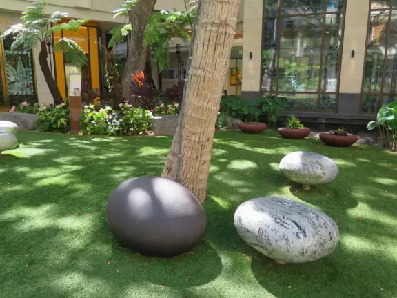 An outdoor mall under a huge banyan tree hung with lanterns. Beautiful flowers by a stream, rock-like seats kids love, and rain fountain.