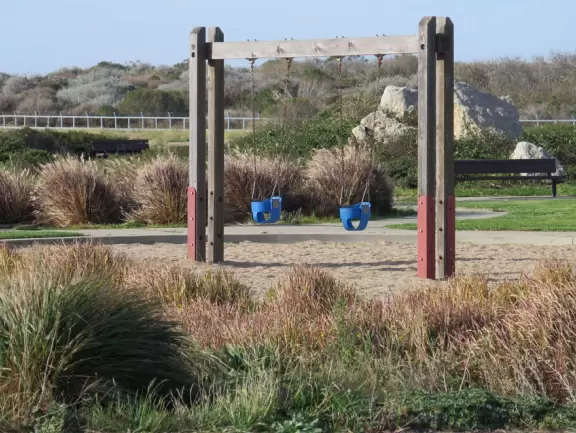 Wide open park behind the dunes in Morro Bay, with play structure with sand floor, and huge lawn with winding paths for tricycling.