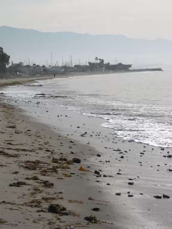 A crescent-shaped beach with rock pools, yellow and white cliffs, and surfers riding small waves near to shore. <br /><br />