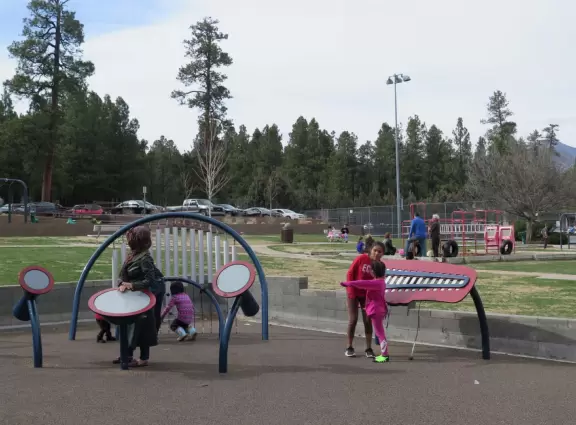 Tons of play structures and equipment in a pretty park with lots of trees.