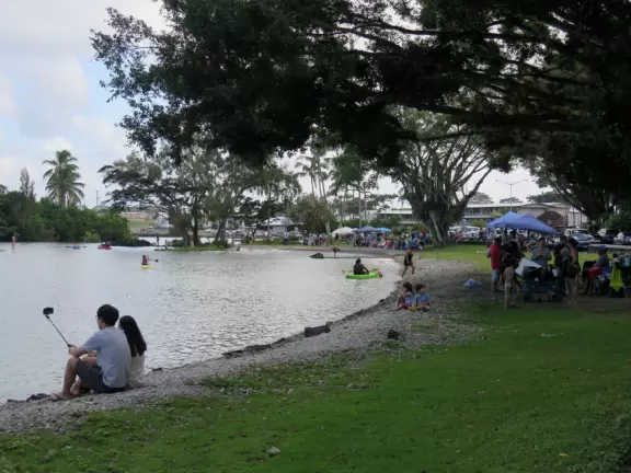 Boats and kayaks in the water, while local families have big gatherings on the grass.