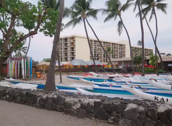 Pier with crystal clear water and views of the church steeple and high mountains backing the bay. Calm cove with Hawaiian hei'au out in the water.