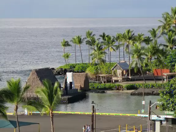Pier with crystal clear water and views of the church steeple and high mountains backing the bay. Calm cove with Hawaiian hei'au out in the water.