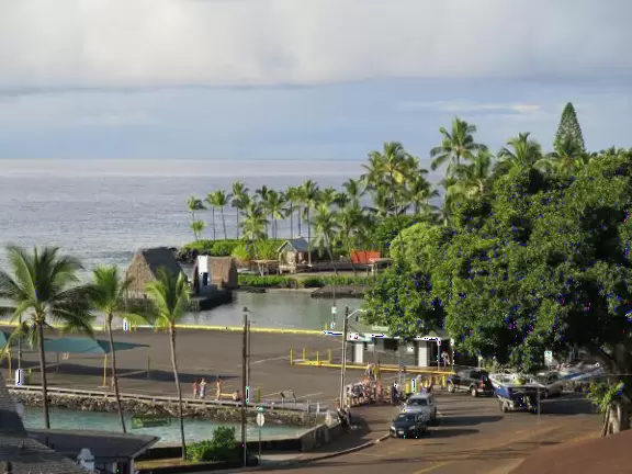 Pier with crystal clear water and views of the church steeple and high mountains backing the bay. Calm cove with Hawaiian hei'au out in the water.