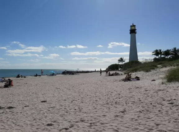 Picturesque beach with white lighthouse, happy people, and turquoise water.