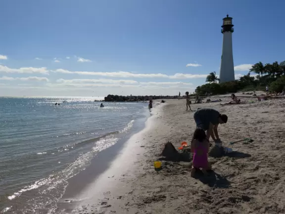 Picturesque beach with white lighthouse, happy people, and turquoise water.