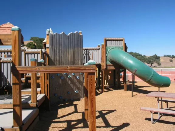 A wooden castle playground with gingerbread house, medieval towers, slides, bridges, monkey bars, rope bars, swings of all sorts, mist maker, viking ship, windmill, wild west town, rock-climbing wall, and tire swing.