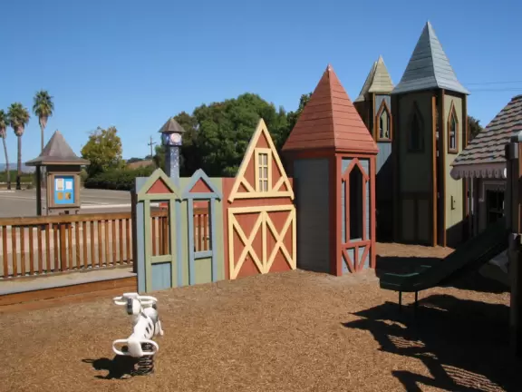 A wooden castle playground with gingerbread house, medieval towers, slides, bridges, monkey bars, rope bars, swings of all sorts, mist maker, viking ship, windmill, wild west town, rock-climbing wall, and tire swing.