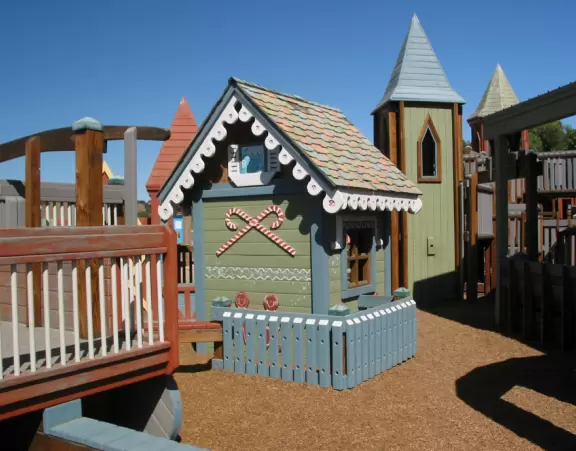 A wooden castle playground with gingerbread house, medieval towers, slides, bridges, monkey bars, rope bars, swings of all sorts, mist maker, viking ship, windmill, wild west town, rock-climbing wall, and tire swing.