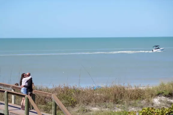 Cozy stretch of white sand with shells and pale green water.