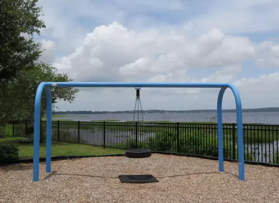 Small strip of land between bike path and lake, with fenced playground and pier.