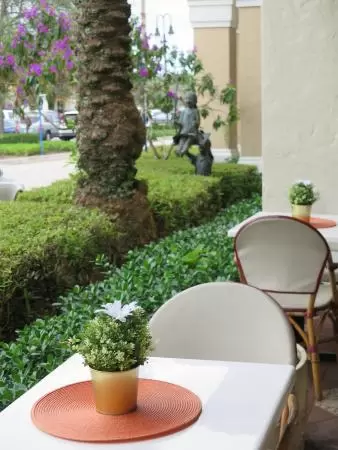 Small shopping plaza with attractive landscaping and design, and beautiful bar area with yellow chairs and tables, fountains, and flowers.