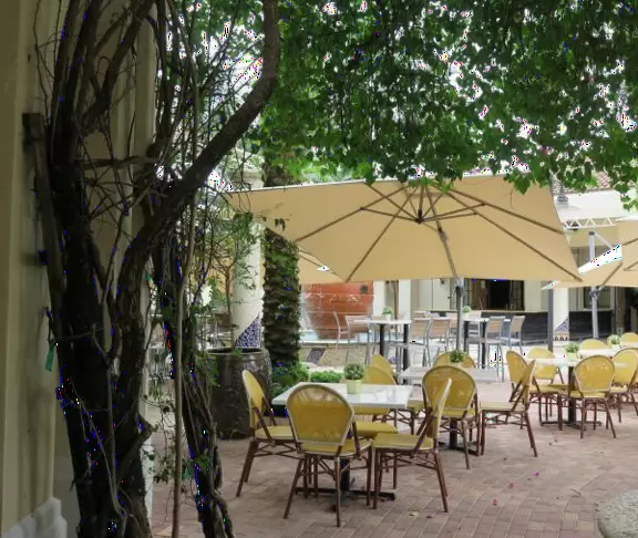 Small shopping plaza with attractive landscaping and design, and beautiful bar area with yellow chairs and tables, fountains, and flowers.