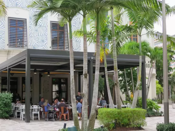 Outdoor shopping and entertainment district with European architecture, archways, palms, tropical flowers, and amazing fountain for kids.