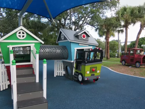 Park with plenty of benches in the shade, accessible playground with unusual equipment, tire swing, dome climby, wooden truck, dinosaur and dolphin bouncy, and plenty of swings.