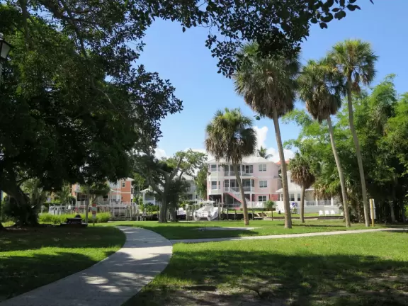 Waterfront park with boardwalk and benches facing the sunset, plus playground under a huge shady canopy and swings over white sand.