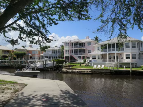 Waterfront park with boardwalk and benches facing the sunset, plus playground under a huge shady canopy and swings over white sand.