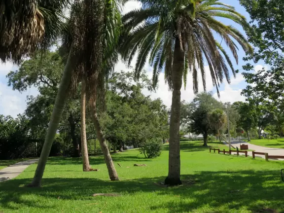 Waterfront park with boardwalk and benches facing the sunset, plus playground under a huge shady canopy and swings over white sand.