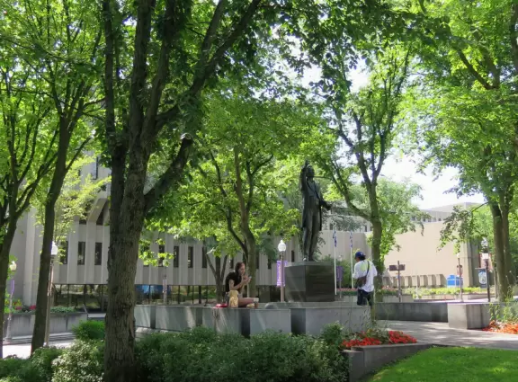 Impressive, stately building atop a hill, with lovely gardens and statues, and a fountain in the middle if the street.