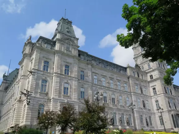 Impressive, stately building atop a hill, with lovely gardens and statues, and a fountain in the middle if the street.