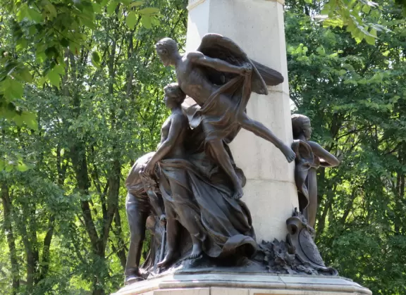 Impressive, stately building atop a hill, with lovely gardens and statues, and a fountain in the middle if the street.