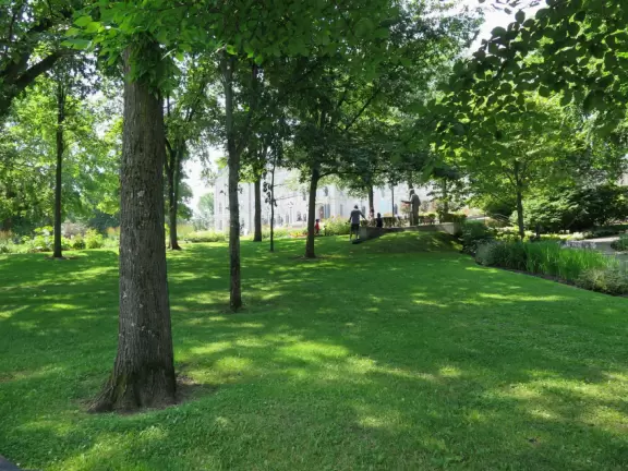 Impressive, stately building atop a hill, with lovely gardens and statues, and a fountain in the middle if the street.