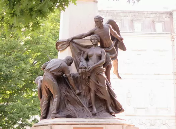 Impressive, stately building atop a hill, with lovely gardens and statues, and a fountain in the middle if the street.