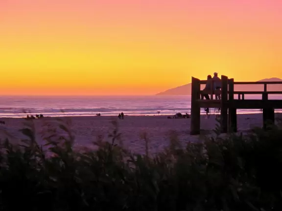 A glorious beach in Grover Beach town, with sand dunes and a wooden boardwalk, plus an octagon-shaped wooden pier in the sand.