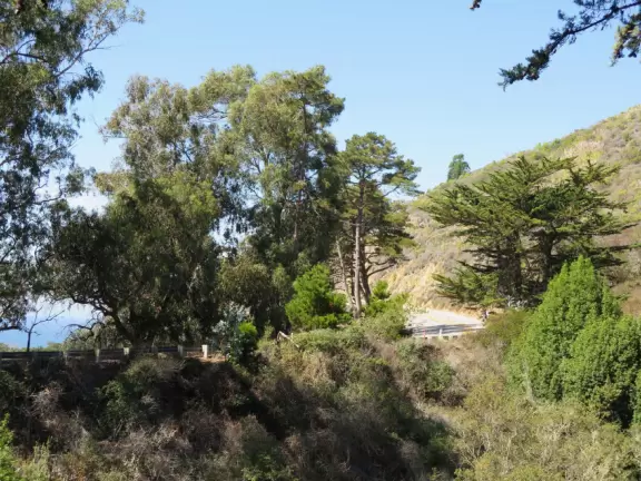 A stunning hike overlooking a white sand beach, bright blue-green waters, and a waterfall falling onto the beach.