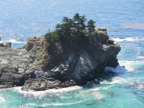 A stunning hike overlooking a white sand beach, bright blue-green waters, and a waterfall falling onto the beach.