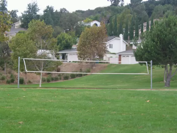 A park with flowering trees, cute playground, basketball courts, volleyball net, and mountain views.