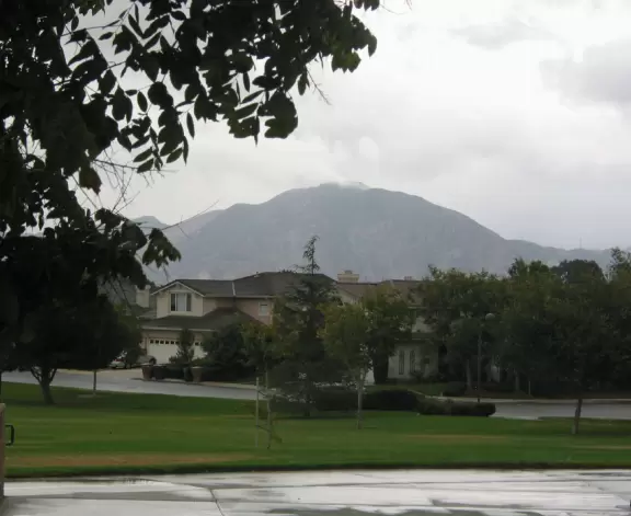 A park with flowering trees, cute playground, basketball courts, volleyball net, and mountain views.