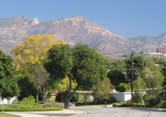 A neighborhood park with close-up views of the mountains. large lawn, playground, autumn trees, and bridge over creek to school.