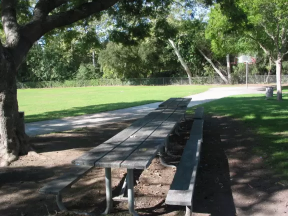 A neighborhood park with close-up views of the mountains. large lawn, playground, autumn trees, and bridge over creek to school.