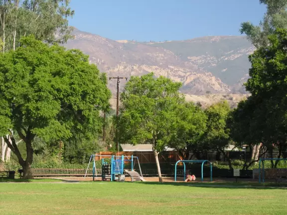 A neighborhood park with close-up views of the mountains. large lawn, playground, autumn trees, and bridge over creek to school.
