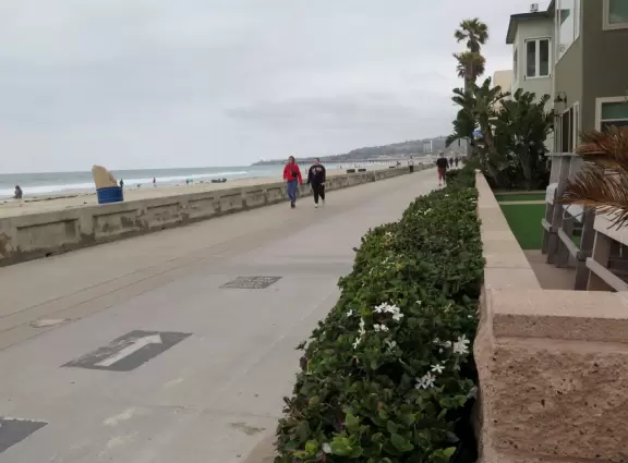 Boardwalk along a fairly grotty beach, where people rollerblade and stroll together.