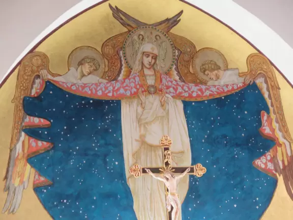 White-washed church with bell towers, rose window, Mary and contented baby Jesus sculpture.