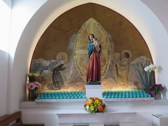 White-washed church with bell towers, rose window, Mary and contented baby Jesus sculpture.