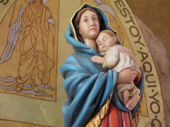 White-washed church with bell towers, rose window, Mary and contented baby Jesus sculpture.