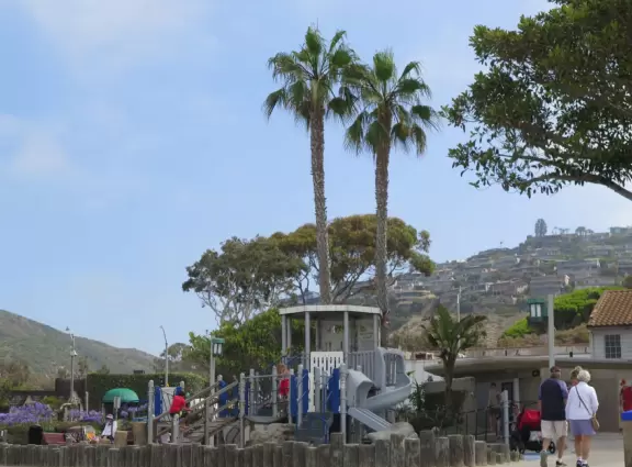 Fun beach with many spots to explore, including rock pools, a walking path with flowers above the sea, basketball courts, a playground, and a lawn by the beach.